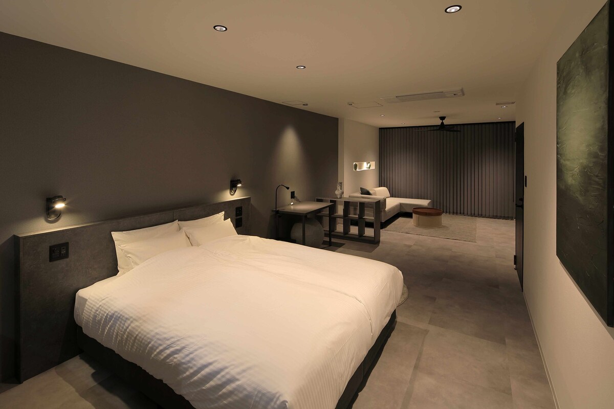 A modern hotel room with a large bed, a desk with a chair, a small table, and a ceiling fan.