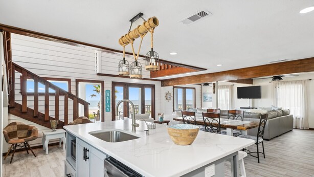 A spacious living area with a large island, a dining table, and a staircase leading to a balcony. - Family Reunions, Corporate/Church Retreats, Large Gatherings-Steps to the beach! (Freeport)