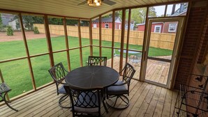 A covered patio with a round table and chairs, large windows, and a view of a backyard. - Remodeled Bungalow walking distance to Augusta National (Augusta)