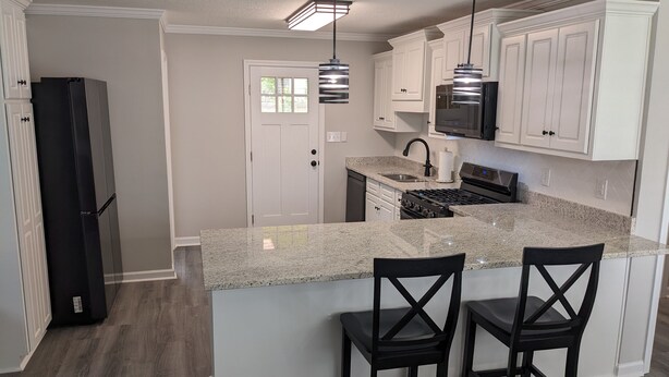 A modern kitchen with white cabinets, a granite countertop, stainless steel appliances, and two black bar stools. - Remodeled Bungalow walking distance to Augusta National (Augusta)