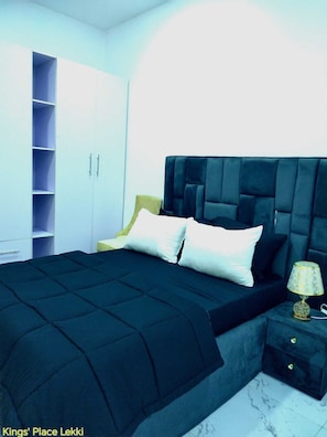 Un dormitorio con cama, mesita de noche, lámpara, armario y estantería.