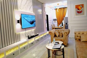 Un salon moderne avec un téléviseur à écran plat fixé au mur, un canapé confortable, une table basse et, au fond, un coin repas.