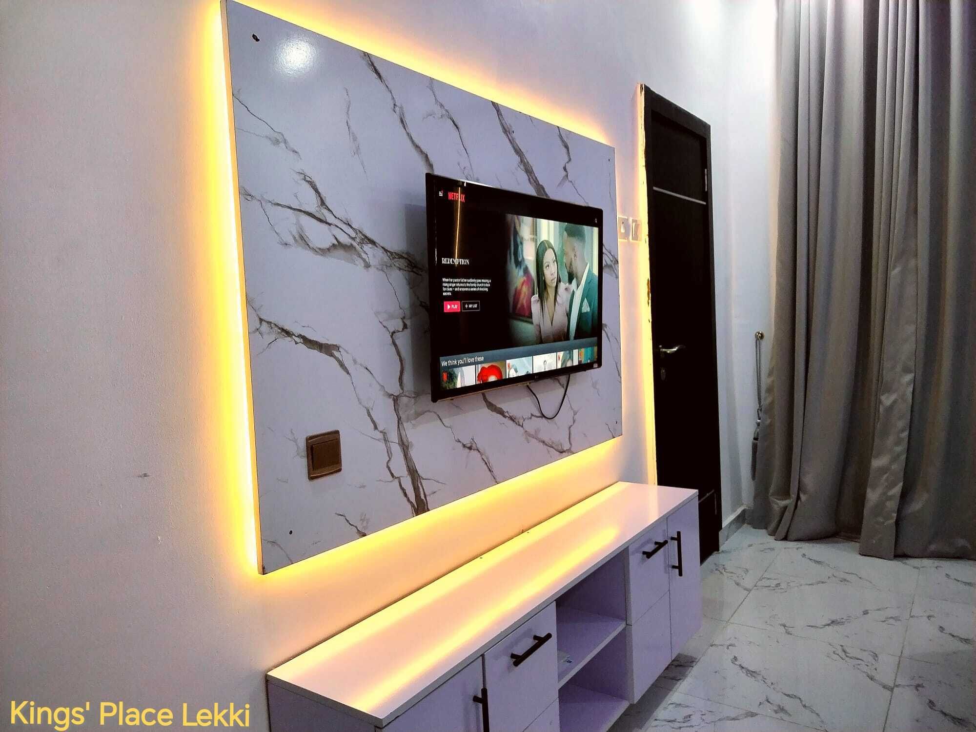 Un salon moderne avec un mur en marbre, un téléviseur à écran plat fixé au-dessus d’une console blanche et une porte donnant sur une autre pièce.