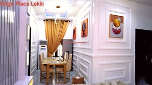 A dining area with a table and chairs, a ceiling light fixture, and a wall-mounted air conditioning unit. - Kings' Place Lekki - 2Bedrooms (Lekki)