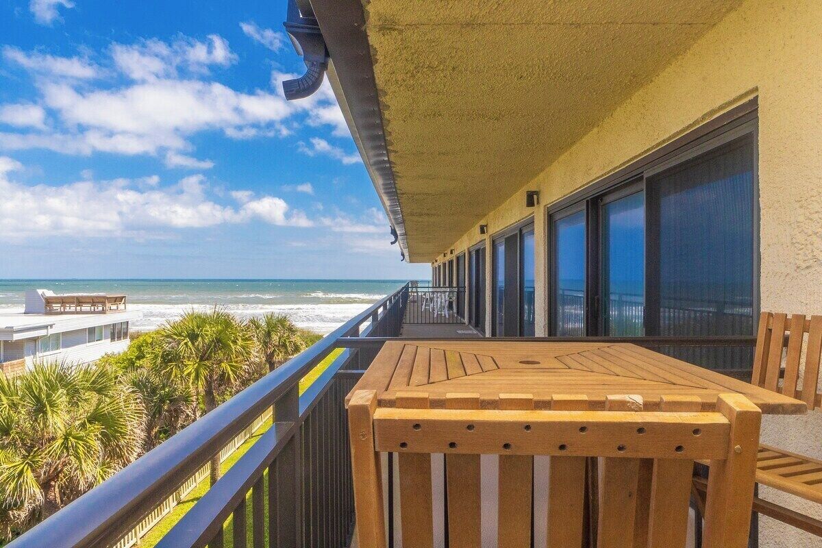 A balcony with a view of the ocean, wooden furniture, and a railing.