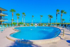 Una piscina con una marca de profundidad de 2.1 metros, rodeada de sillas de descanso y palmeras, con un edificio al fondo.