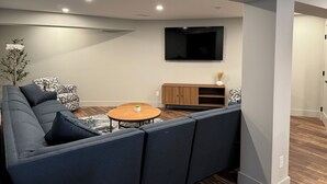 Ein modernes Wohnzimmer mit einer Eckcouch, einem runden Couchtisch, einem an der Wand befestigten Fernseher und einem Holzschrank.