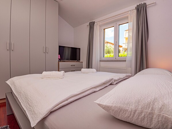 A bedroom with two beds, a TV, and a window with curtains.