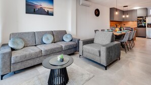 A modern living room with a grey sofa set, a round coffee table, and a dining area with a wooden table and chairs.