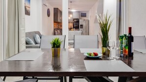 A modern dining area with a table set for two, a potted plant, a plate of fruit, and a bottle of wine.