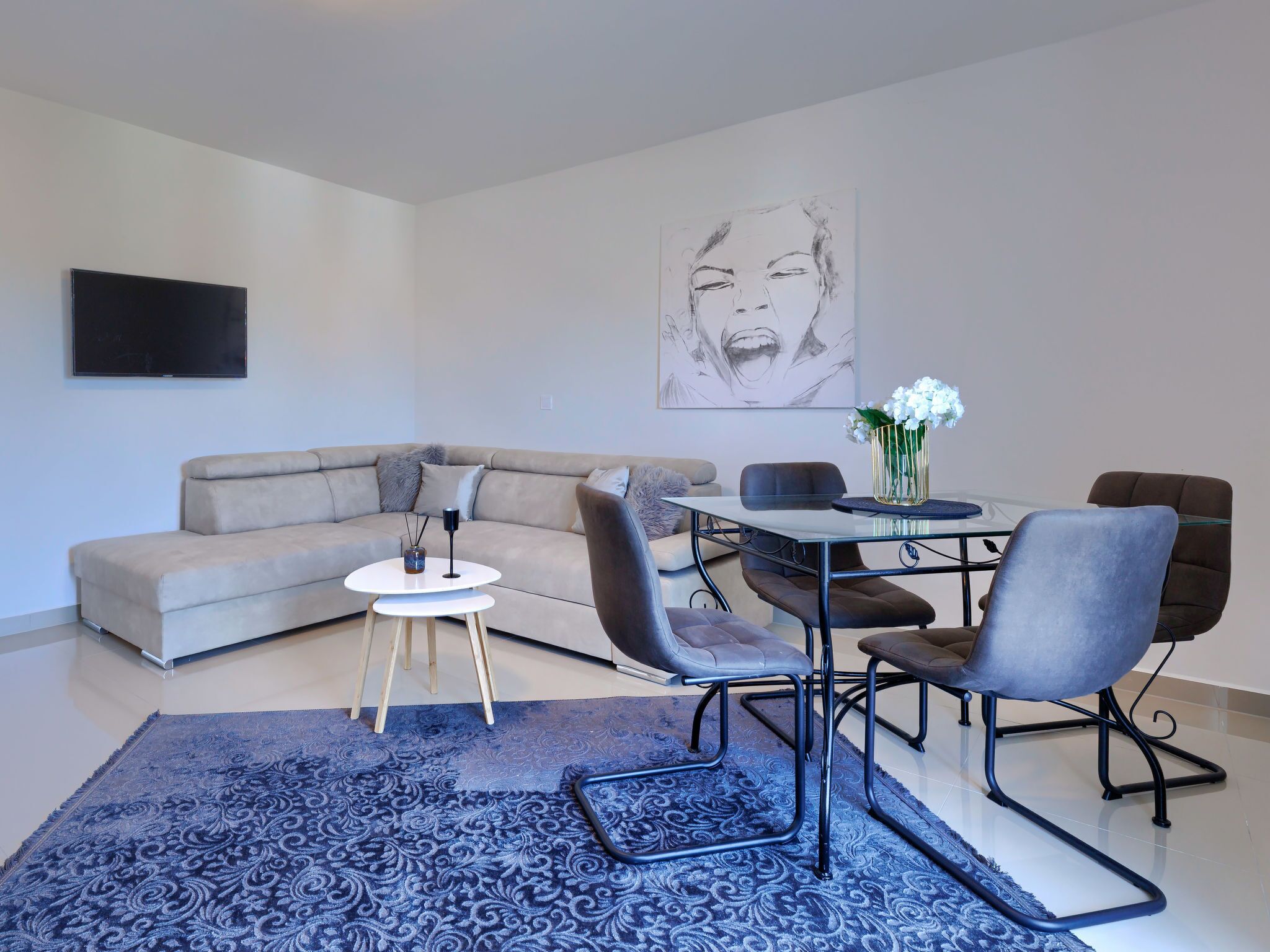 Uma sala de estar moderna com sofá seccional, mesa de jantar com cadeiras, mesa de centro e uma grande pintura abstrata.