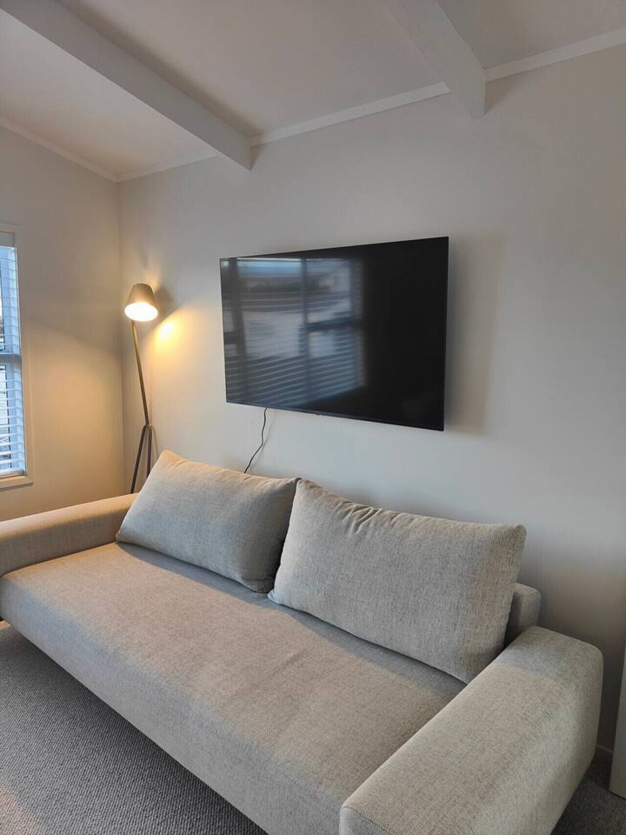 A modern living room with a grey sofa, a mounted flat-screen TV, and a floor lamp.