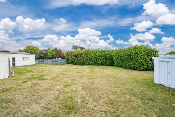 A backyard with a white shed, a wooden fence, and a hedge.