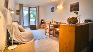 A cozy living room with a sofa, a wooden dining table with chairs, a coffee table, and a small kitchen area with a fruit bowl and a kettle. - l'Oasis by Interhome (Ile d'Oléron)