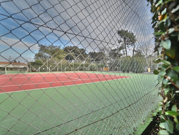 A tennis court enclosed by a chain-link fence with a green surface and red boundary lines.