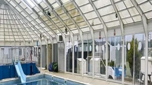 Une piscine intérieure dotée d’un toit en verre, d’une eau cristalline et d’un toboggan bleu.