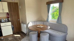 Ein gemütlicher Wohnbereich mit Küchenzeile, einem grauen Sofa, einem runden Holztisch und einem Fenster mit Blick ins Grüne.