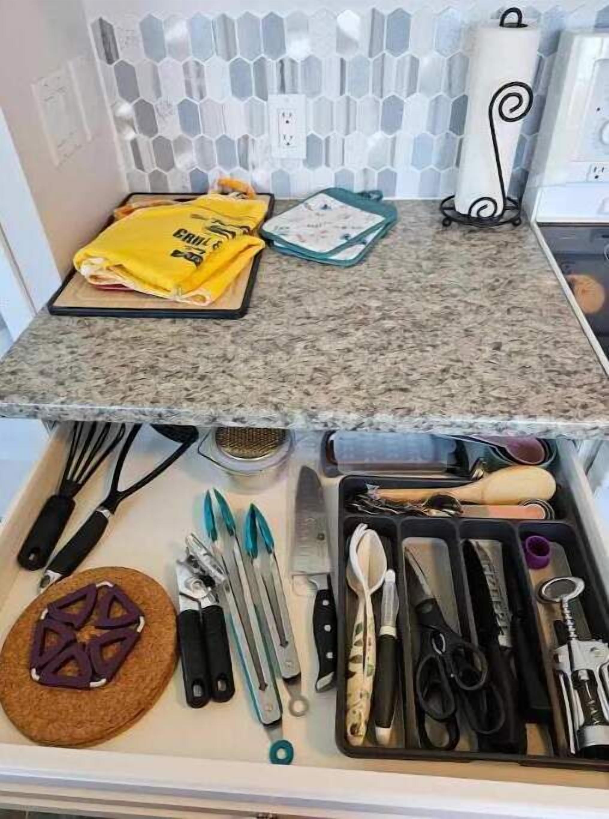 Una cocina con encimera de granito, un paño amarillo y un cajón con diferentes utensilios.