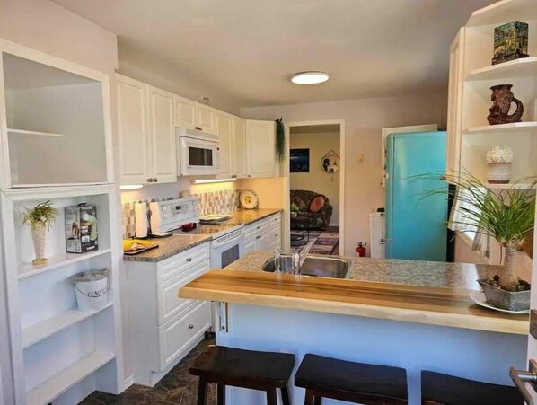 A compact kitchen with white cabinets, a microwave, a sink, and a small island with stools.