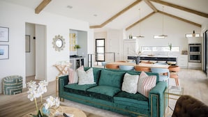 Un salón espacioso con un sofá verde, vigas de madera y una cocina al fondo.