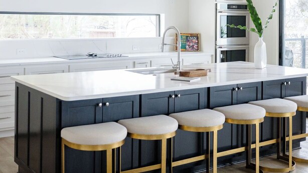 Una cocina moderna con una isla grande, taburetes de bar, iluminación colgante y vistas al exterior.