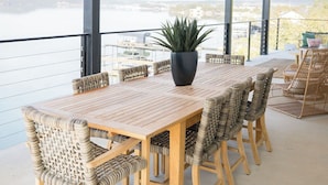 Un espacio al aire libre cubierto con área de comedor, una mesa de madera y sillas de mimbre, una planta en maceta y vistas de la ciudad.