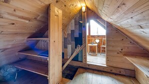 Interior de madera con una escalera que sube a un nivel superior, un abanico y una mesita con una silla.