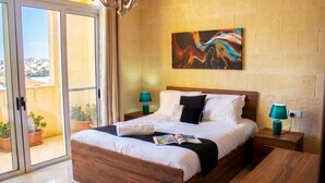A bedroom with a bed, two bedside tables, a painting on the wall, and a view through a sliding door. - Kenn Gozitan villa and pool, L-Gharb Gozo, Malta (L-Gharb Gozo)
