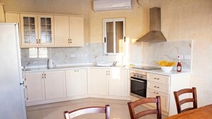 A kitchen with white cabinets, a stove, and a dining table with chairs. - Kenn Gozitan villa and pool, L-Gharb Gozo, Malta (L-Gharb Gozo)
