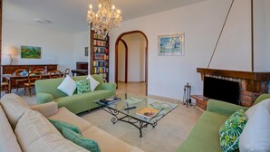 A living room with green sofas, a glass coffee table, a chandelier, a fireplace, and a bookshelf. - Blooming Villa Cos with Garden and Lake View, Belgirate, Italy (Belgirate)