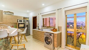 A modern kitchen with a built-in washing machine, dining area with chairs, and a view through a glass door.