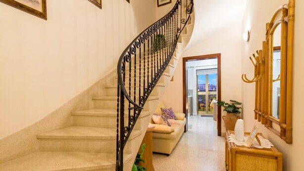 A staircase with a black iron railing, a beige sofa, a wooden side table with a vase, and a mirror on the wall. - Sunny Maltese townhouse Madonnina Kalkara, Kalkara, Malta (Kalkara)