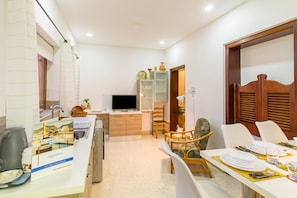 A hotel room with a dining area, a TV, a bookshelf, and a wooden door.
