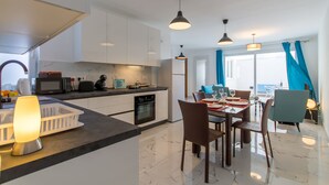 Eine moderne Küche mit weißen Schränken, ein Essbereich mit Tisch und Stühlen sowie Meerblick durch große Fenster.
