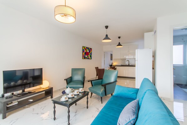 Un salon moderne doté d’un téléviseur à écran plat, de deux fauteuils turquoise, d’un canapé bleu, d’une table basse et de luminaires suspendus.