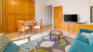 Una sala de estar con televisor, muebles de madera y una alfombra estampada.