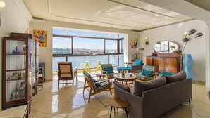 Ein geräumiges Wohnzimmer mit großem Fenster, einer Couch, Sesseln, einem Schrank und einem dekorativen Spiegel.