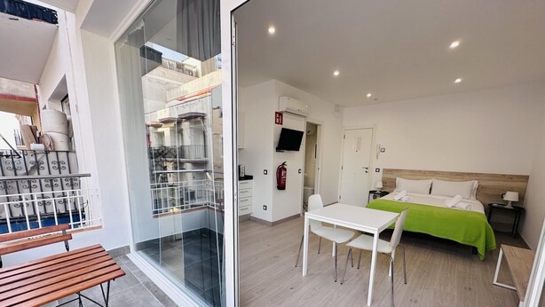 Une chambre d’hôtel moderne dotée d’un balcon, d’un coin repas et d’un lit recouvert d’une couverture verte.