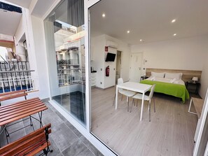 A modern hotel room with a balcony, a dining area, and a bed with a green bedspread. - RAINBOW VERD BY BLAUSITGES (SITGES)
