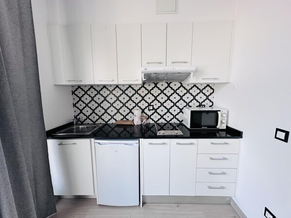 A compact kitchen with white cabinets, a black countertop, a microwave, and a small refrigerator. - RAINBOW VERD BY BLAUSITGES (SITGES)