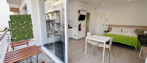 Una habitación de hotel moderna con balcón, zona de comedor y cama con colcha verde.