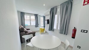 En moderne stue med et rundt hvidt bord og stole, en brun sofa, grå gardiner og en brandslukker på væggen.