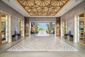 A spacious lobby with a geometric patterned floor, a high ceiling with a geometric design, and a view of an outdoor seating area through a large doorway. - Khao Lak Marriott Beach Resort and Spa  (Takua Pa)