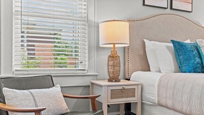 A bedroom with a bed, a bedside table with a lamp, a chair, and a window with blinds.