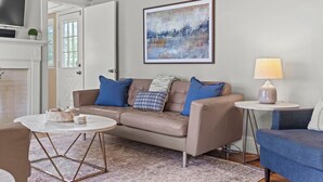 A living room with a beige sofa, a coffee table, a side table with a lamp, and a painting on the wall.
