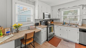 A modern kitchen with white cabinets, a granite countertop, a stove, a microwave, and a sink.