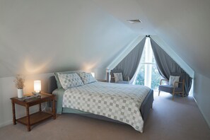 A bedroom with a checkered bedspread, a bedside table with a lamp, and a chair near a window. - The White House-Studio (Metung)