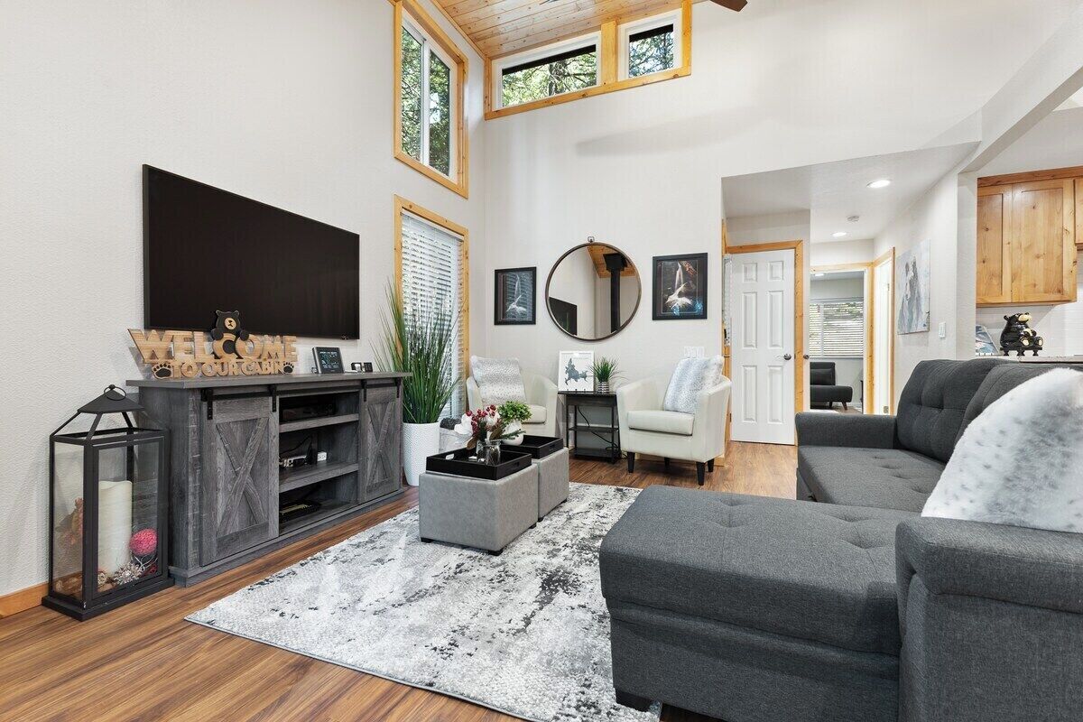 A spacious living room with a grey sofa, a coffee table, and a TV mounted on the wall.