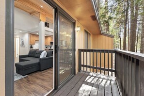Et moderne interiør med en træterrasse, en skydedør til en opholdsstue og udsigt til et skovområde.