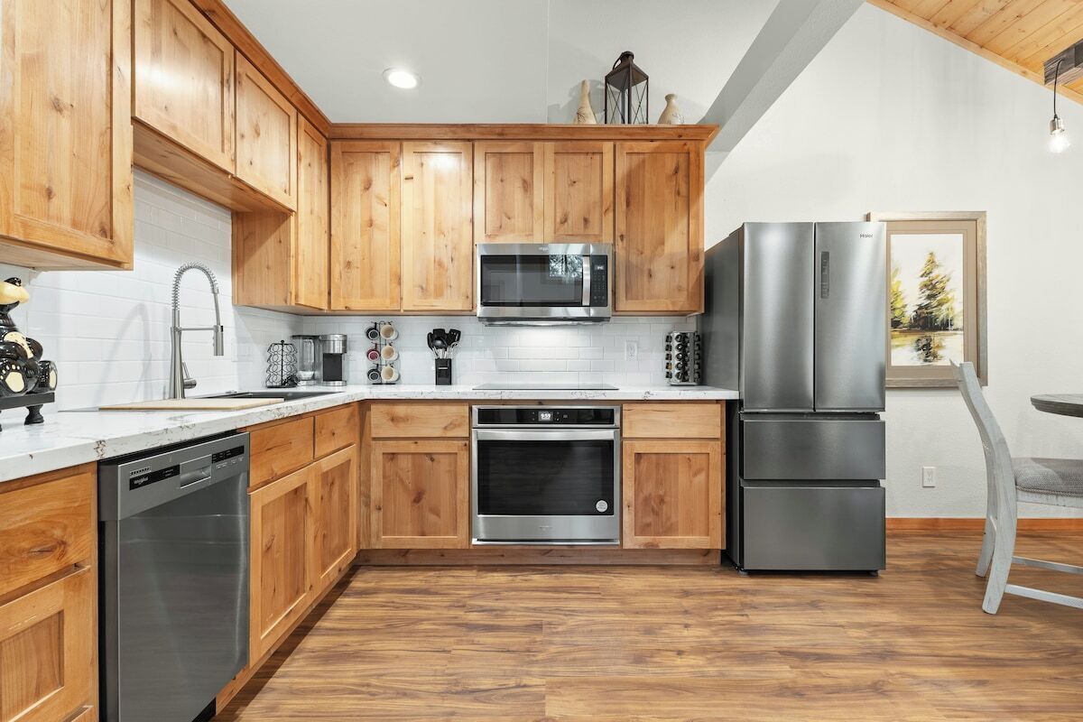 Una cocina con gabinetes de madera, electrodomésticos de acero inoxidable y vistas a árboles a través de una ventana.